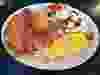 A plate with pancakes, bacon, scrambled eggs and fresh fruit