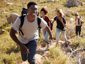 Millennial African American man leading friends hiking single file uphill on a path in countryside