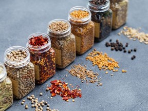 Assortments of spices, white pepper, chili flakes, lemongrass, coriander and cumin seeds in jars on grey stone background. Copy space.