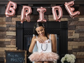 Young smiling woman opening a present at her bridal shower n her home. Pink bride balloons in background