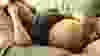 Asian woman pregnant and in distress lying on the couch. Appears tired and uncomfortable.