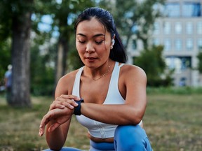 Female athlete setting up smart watch before workout in a forest. Beautiful asian sportswoman checking data on her gadget outdoor.