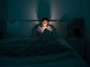 Woman in the dark scrolling through her phone. Woman lying in bed scrolling on phone.