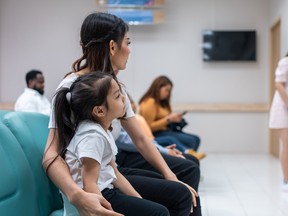 Asian family patient wait on line queue to receive medicine in hospital. Attractive mother and daughter sit on chairs, waiting the pharmacy counter to provides services to patients in medical center.