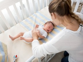 Woman watching over baby in crib.