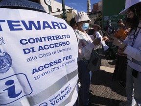 Stewards check tourists' QR codes outside the main train station in Venice, Italy, Friday, April 18, 2025, as the city for a second year is charging day-trippers an arrivals tax. (AP Photo/Antonio Calanni)